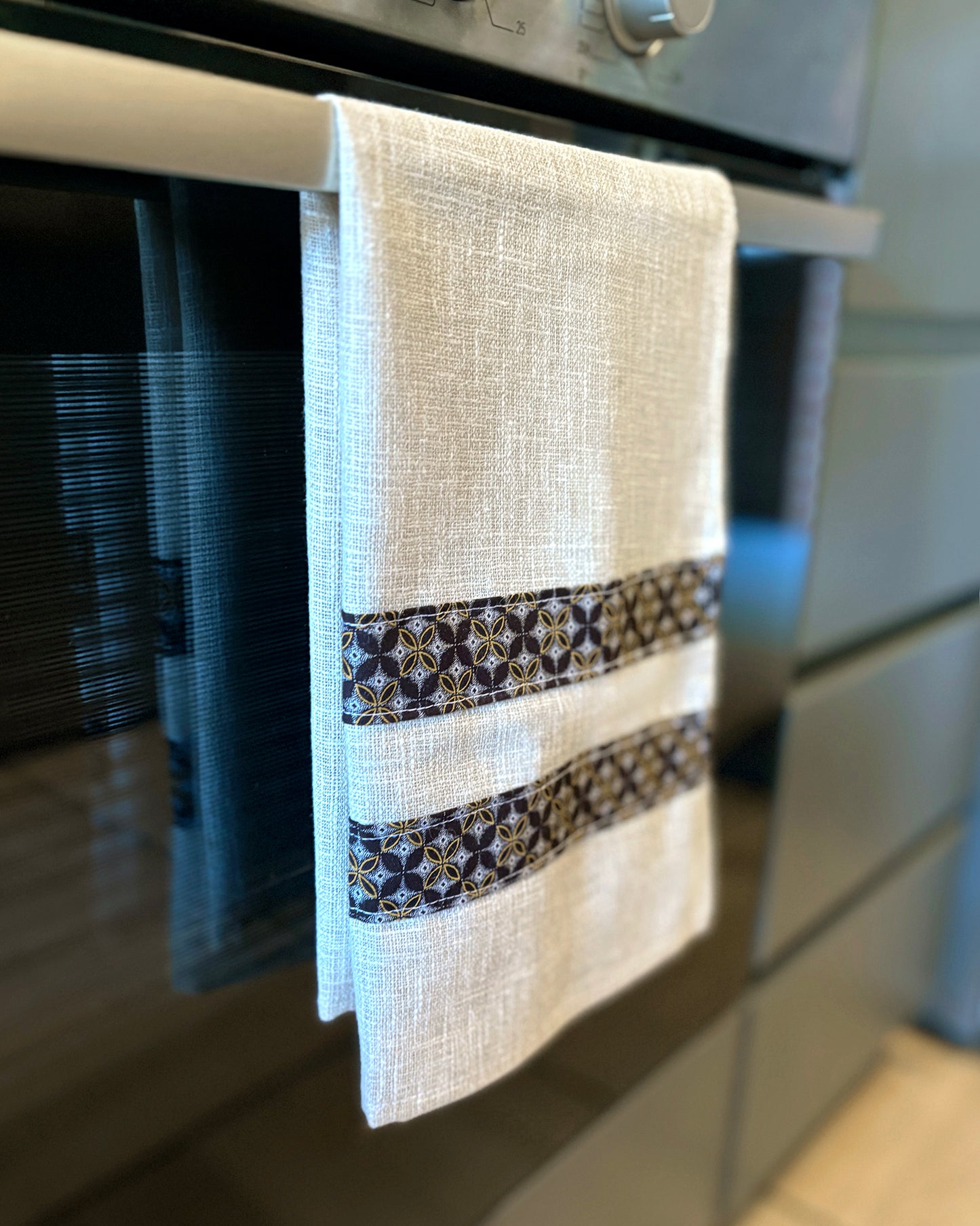 Beige Tea Towel with Brown Geometric Shwe Shwe fabric accents, hanging in front of oven door.