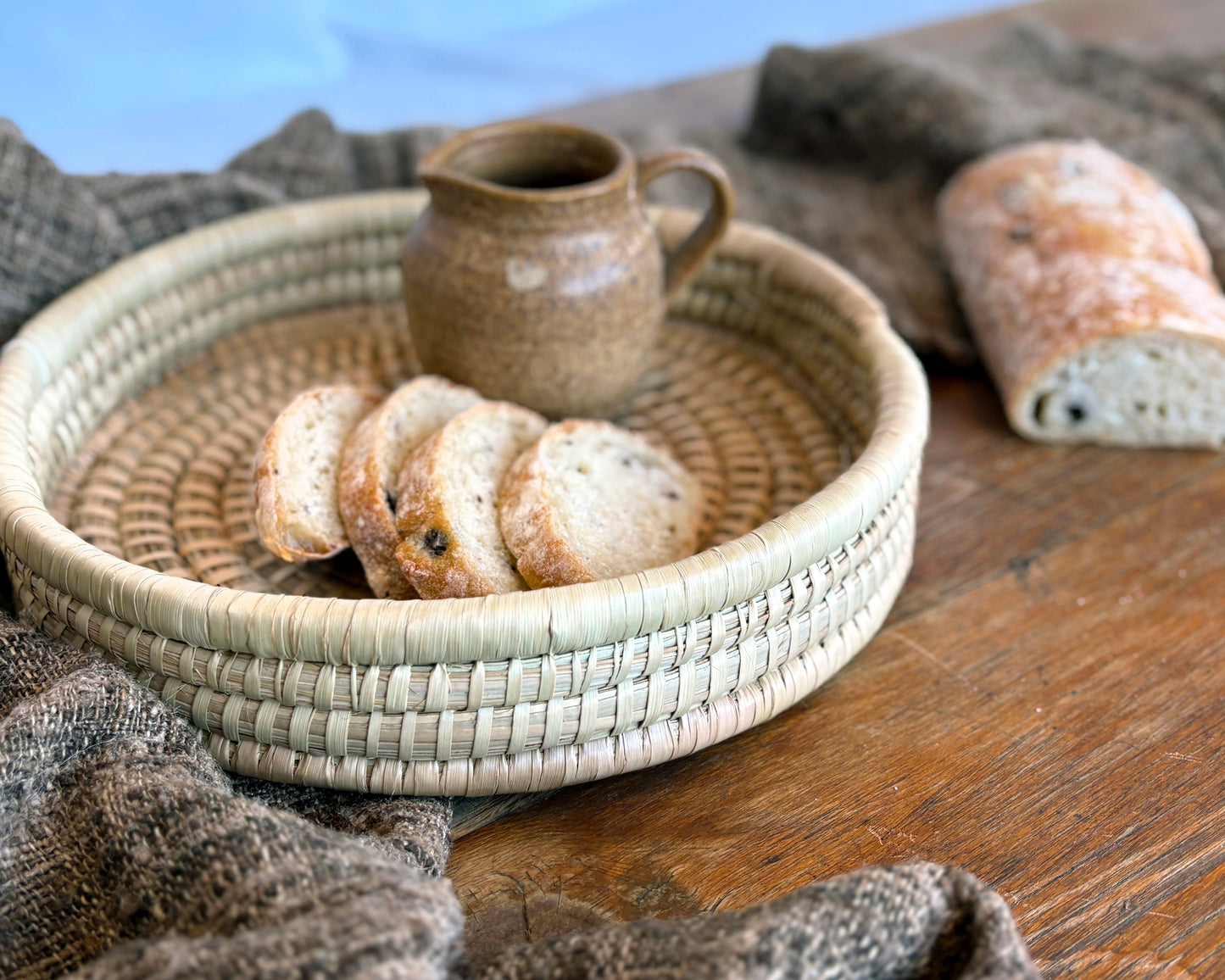 Round Woven basket with bread slices and a ceramic pitcher on a wooden surface