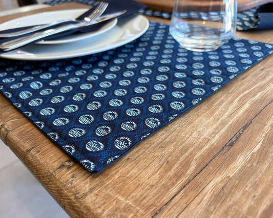 Close up of Blue ShweShwe Fabric placemats with White Protea print on wooden table.