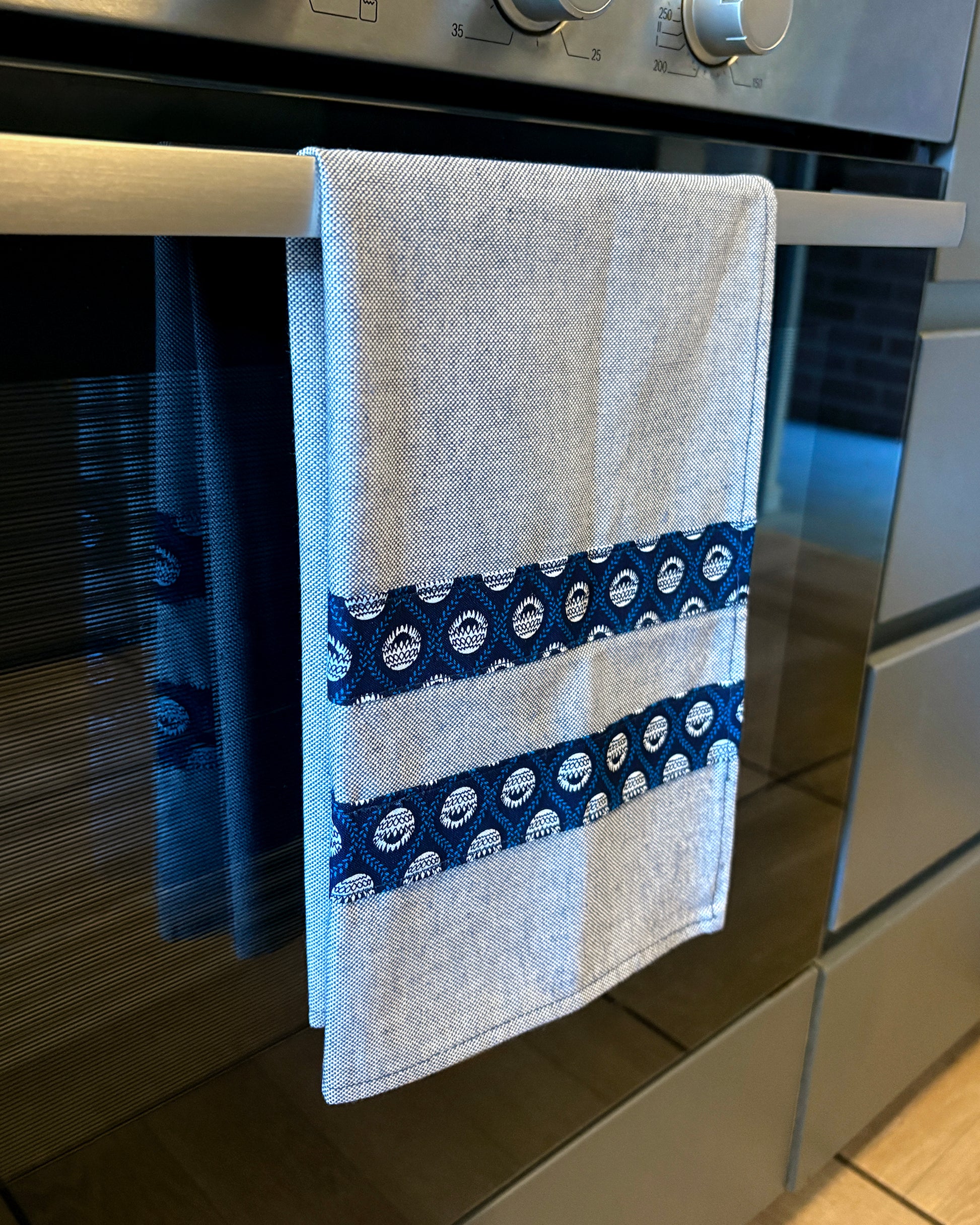 Blue Tea Towel with Protea Shwe Shwe fabric accents, hanging in front of oven door.