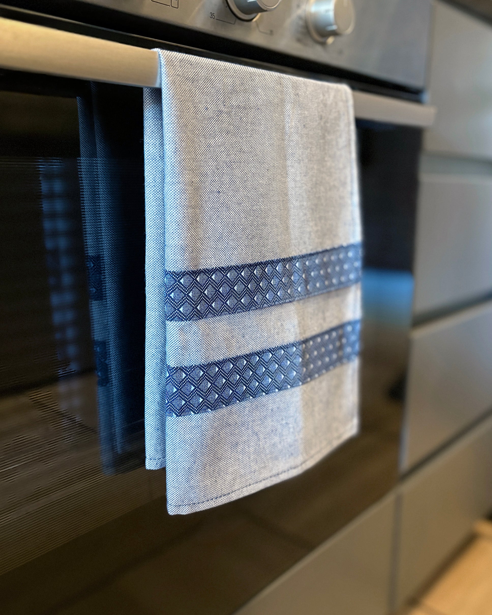 Blue Tea Towel with Diamond Shwe Shwe fabric accents, hanging in front of oven door.