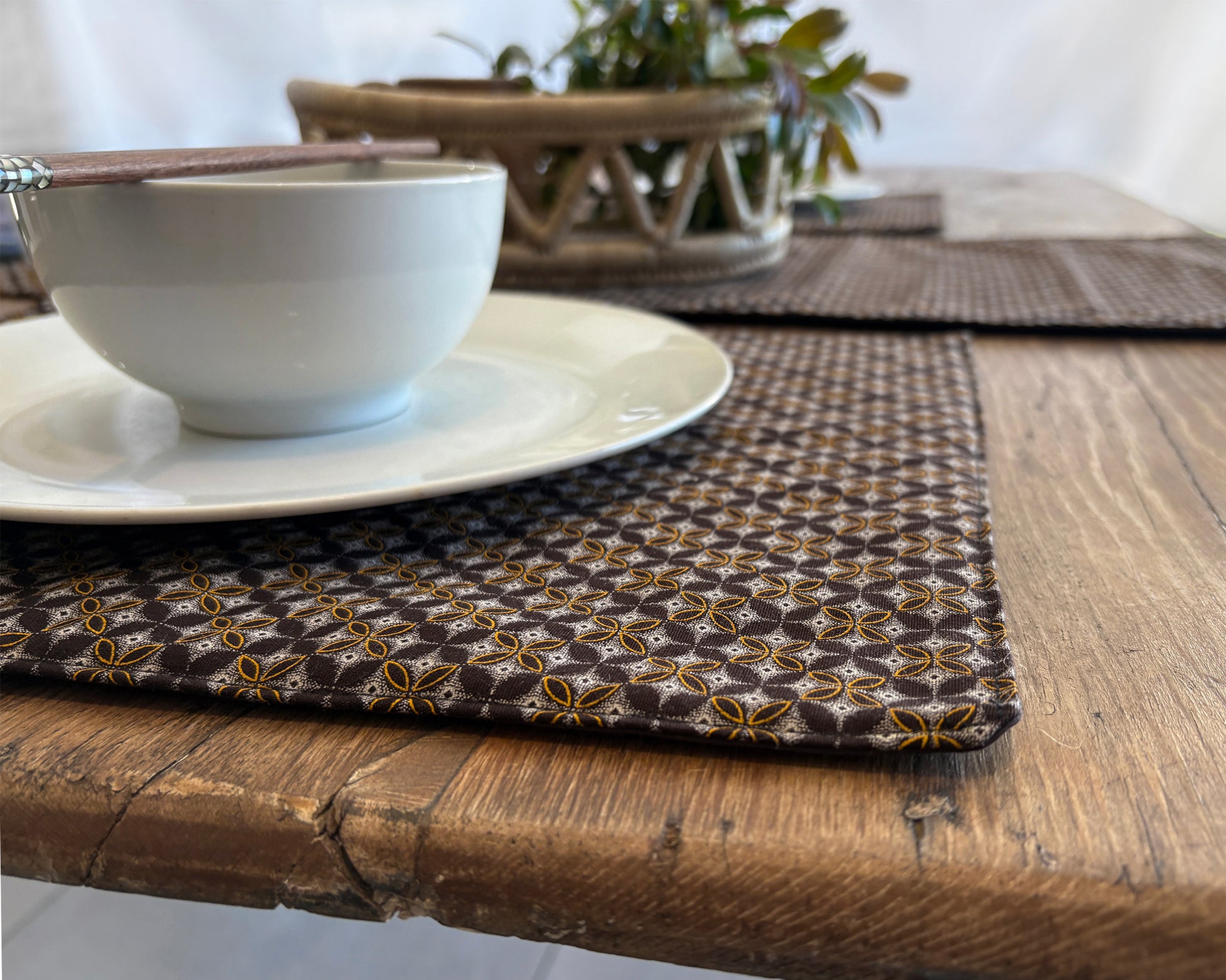 Close up of Brown Shwe Shwe Fabric placemats with White & Yellow Geometric print on wooden table.