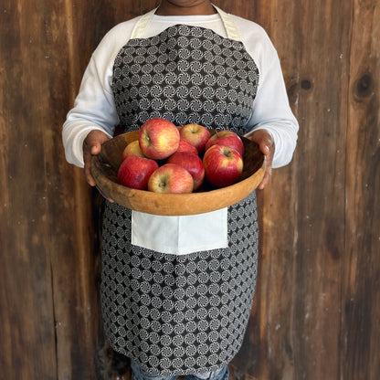 Person wearing a brown patterned Shwe Shwe apron with white front pocket carrying bowl of apples