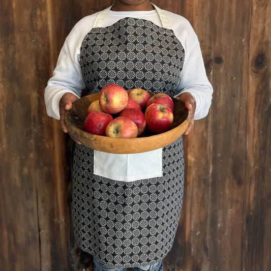 Person wearing a brown patterned Shwe Shwe apron with white front pocket carrying bowl of apples