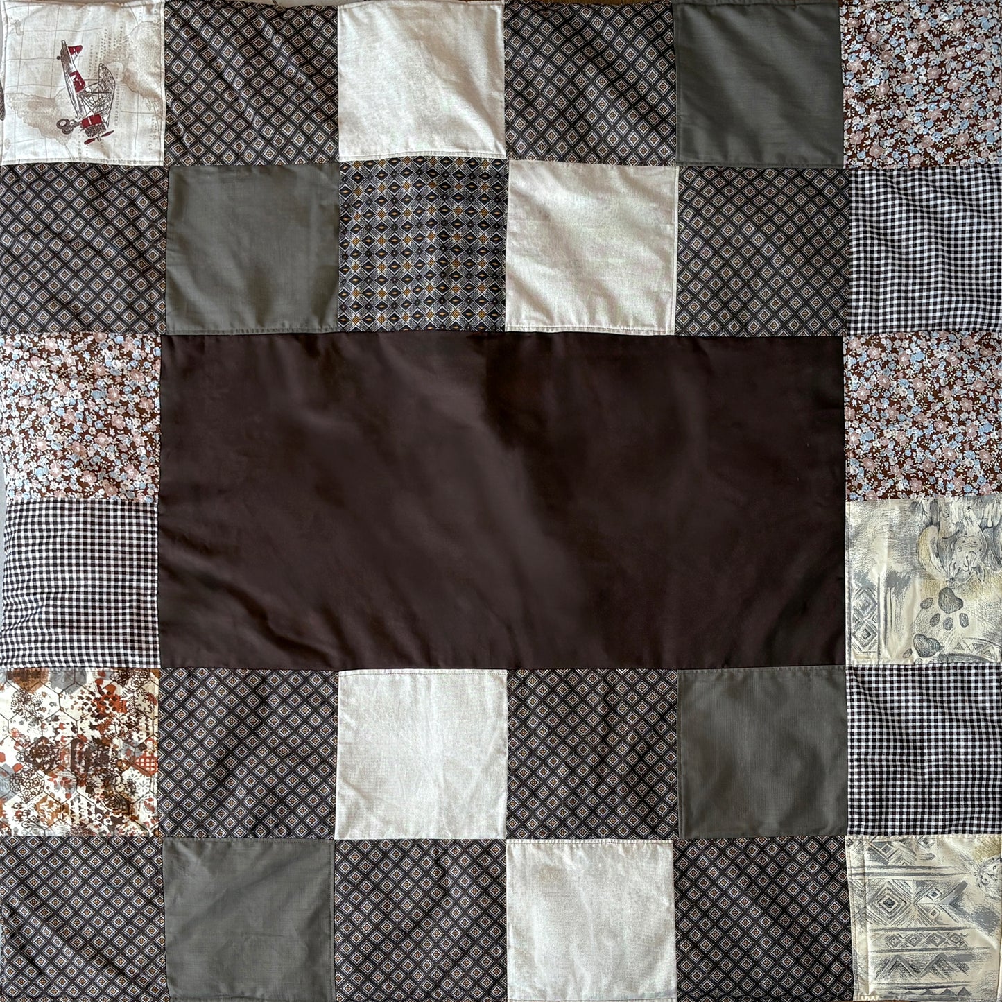 Patchwork picnic blanket with various patterned  brown fabric squares around a plain brown middle inset.