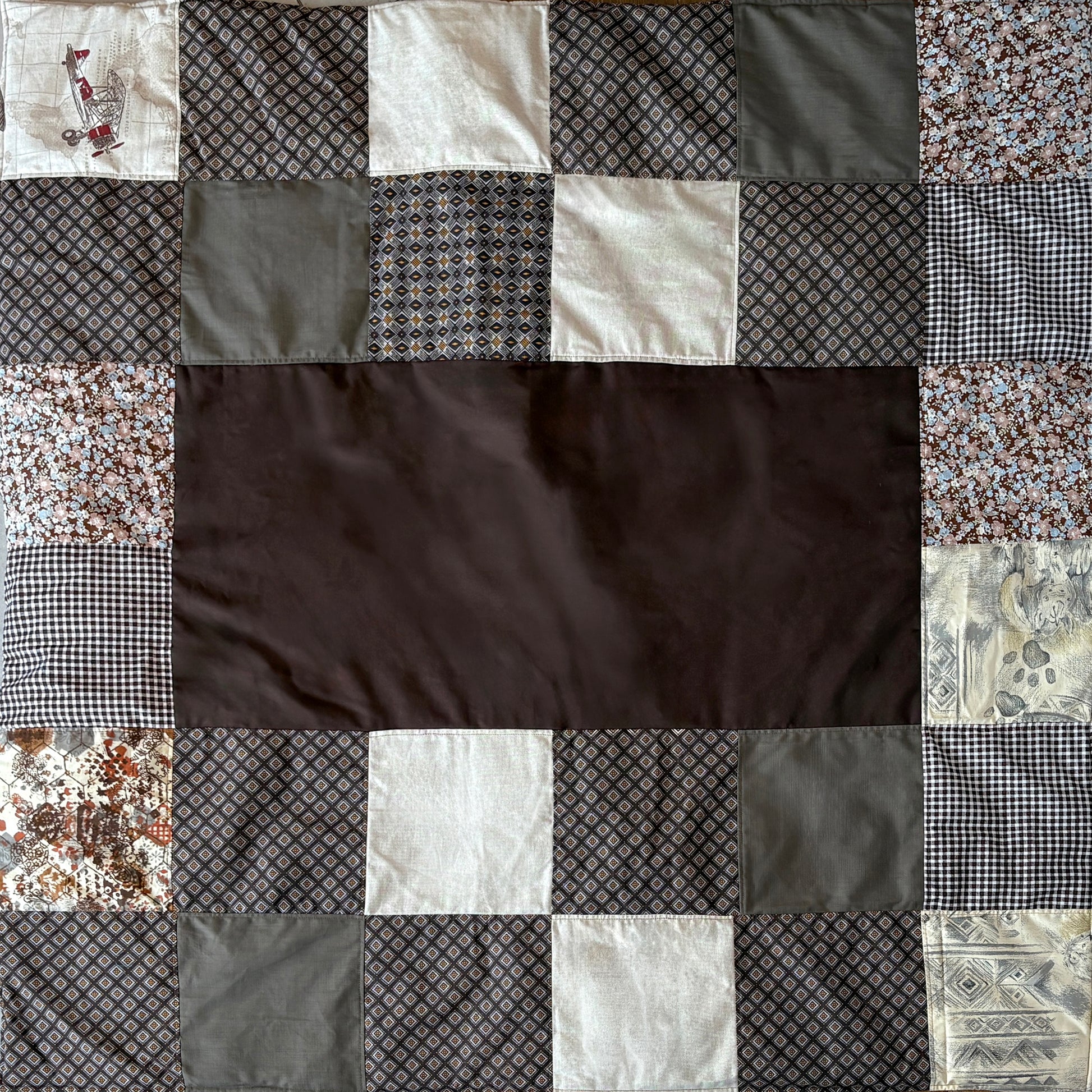 Patchwork picnic blanket with various patterned  brown fabric squares around a plain brown middle inset.