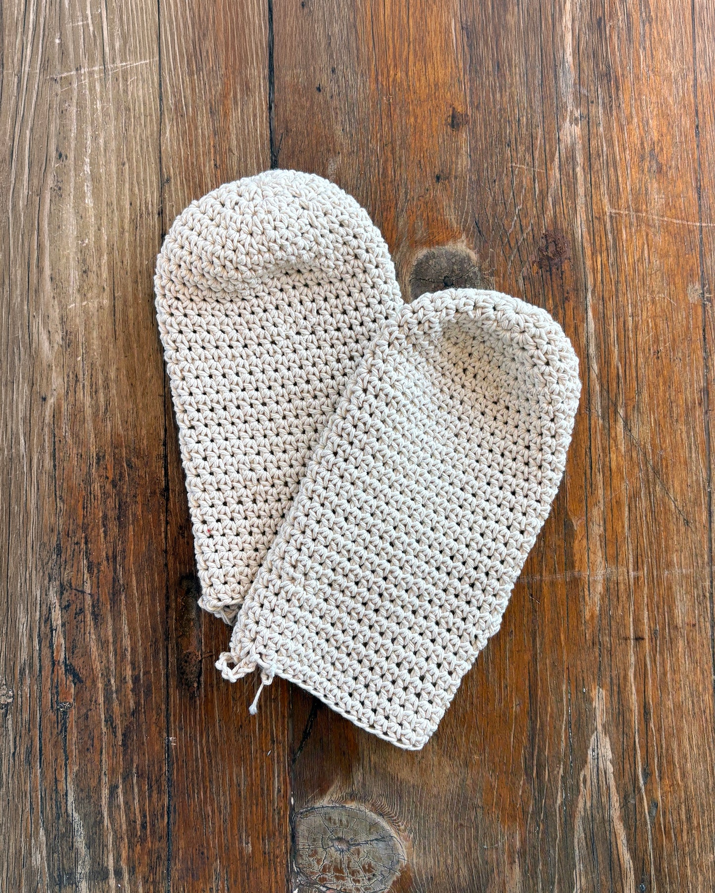 Pair of natural white crochet wash mittens on a wooden surface