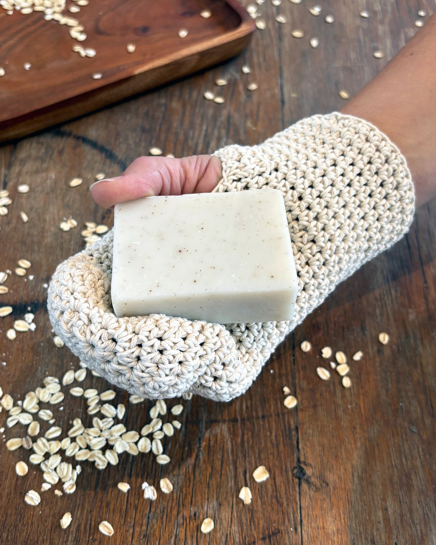 Natural white crochet wash mitt on hand holding soap.