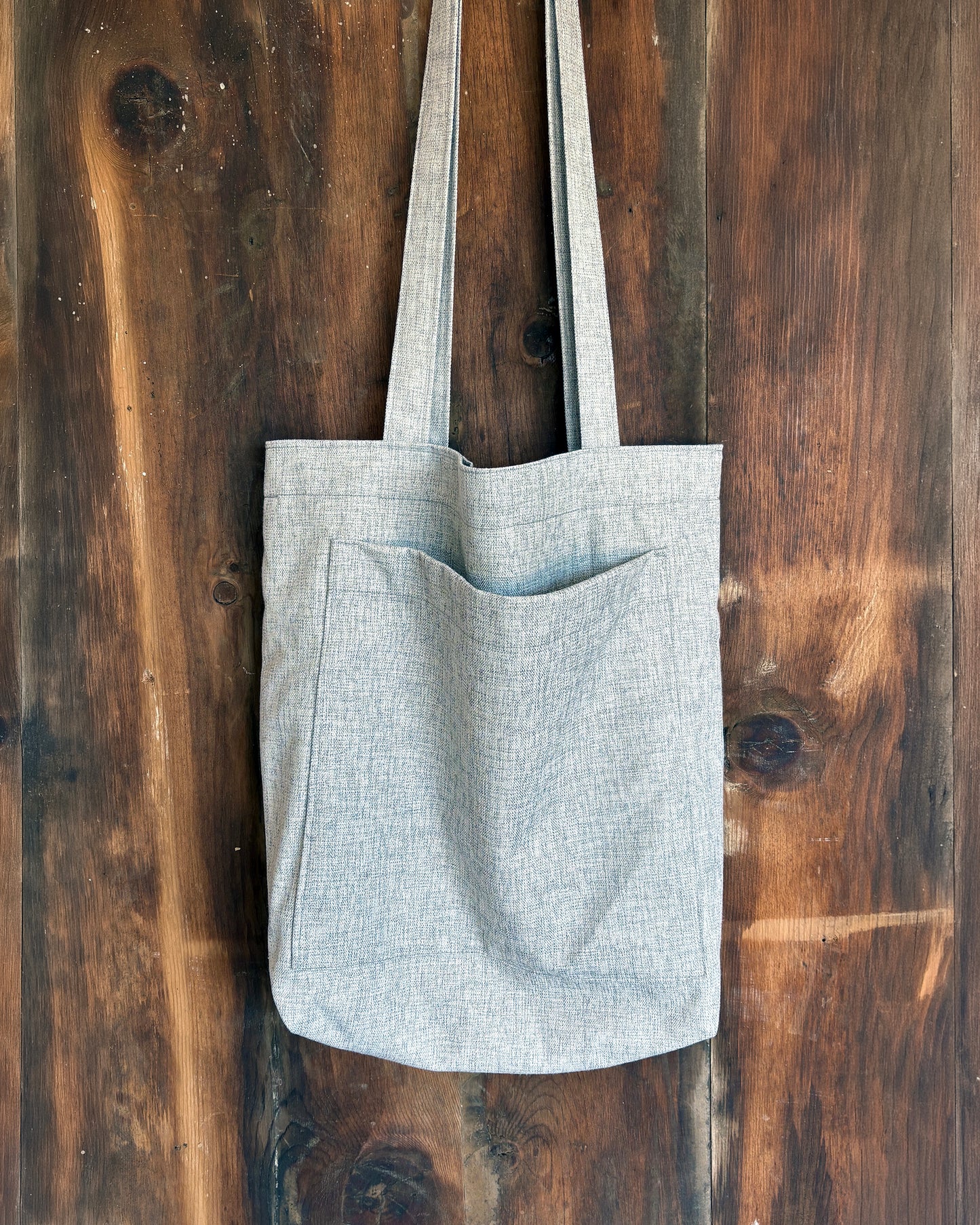 Grey lined tote bag on a wooden surface, with front pocket