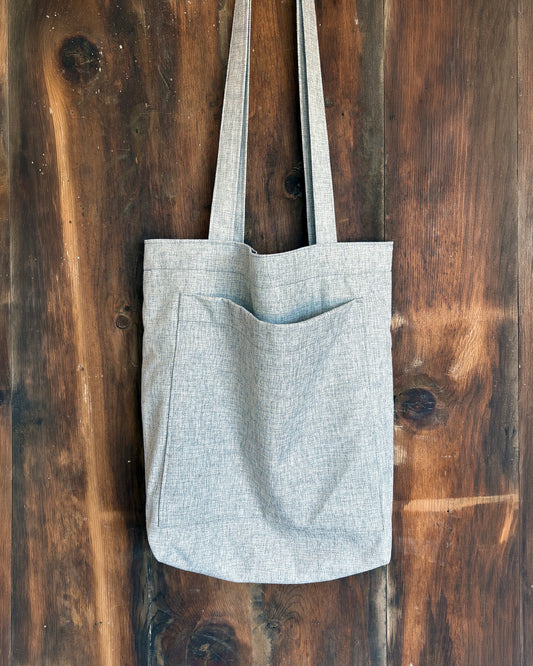 Grey lined tote bag on a wooden surface, with front pocket