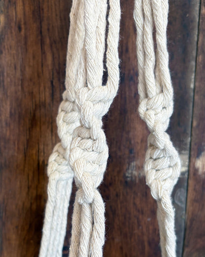 Close-up of a knotted beige rope plant hanger against a wooden background