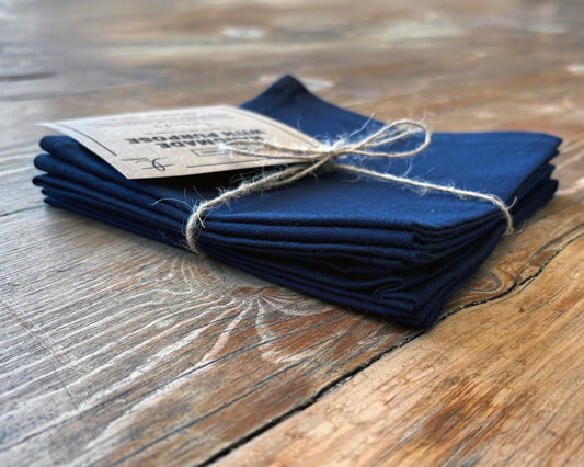 Set of 4 navy blue napkins on a wooden surface. Side view.