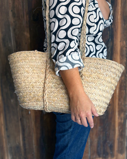 Person holding a woven picnic basket against a wooden background