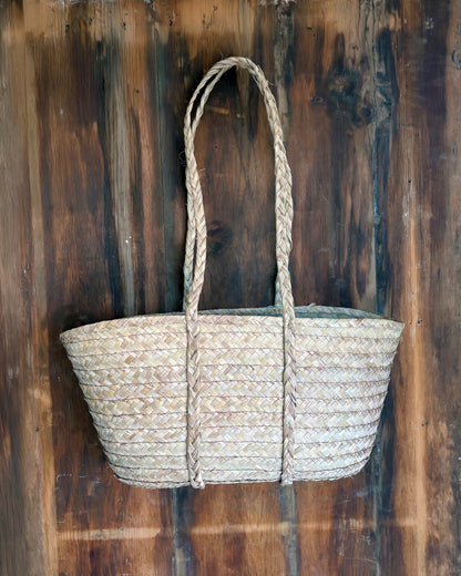 Woven picnic basket with handles hanging against a wooden background